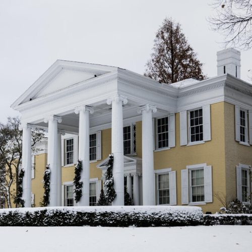 picture of a fancy two story house with yellow walls covered under snow