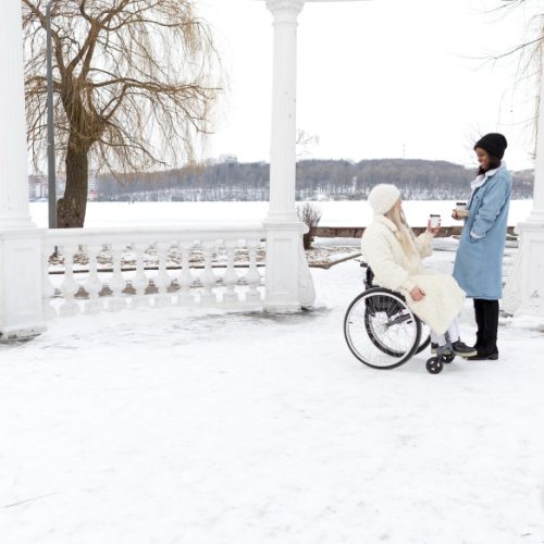 picture of balcony with fancy fences covered by snow and two woman holding coffee cups one of them on wheelchair